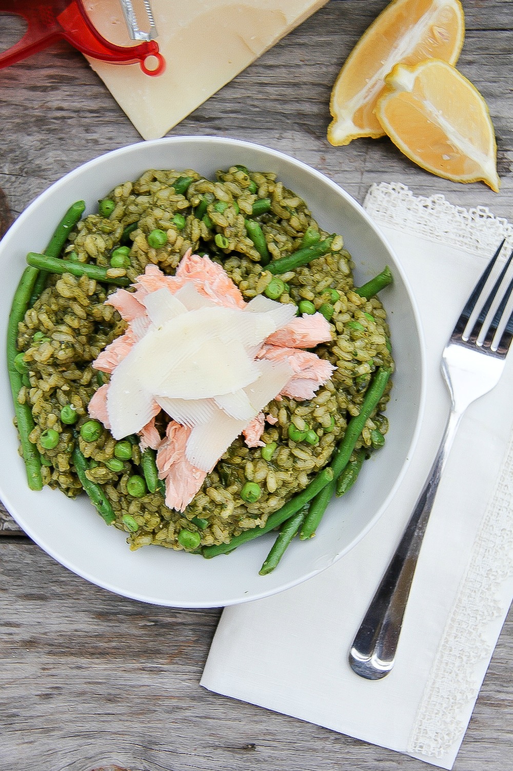 pesto risotto in a white bowl with peas and salmon with cheese