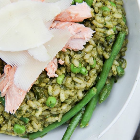 looking down on a white bowl filled with pesto risotto, peas, salmon, and cheese