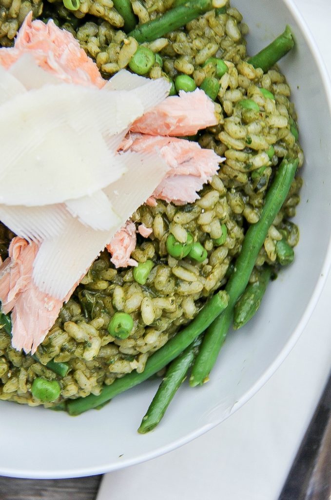 looking down on a white bowl filled with pesto risotto, peas, salmon, and cheese