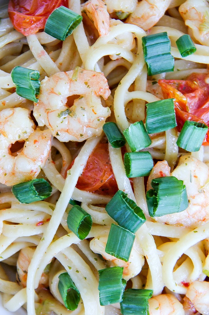 a photo of shrimp scampi up close with shrimp, linguine, green onions, and tomato