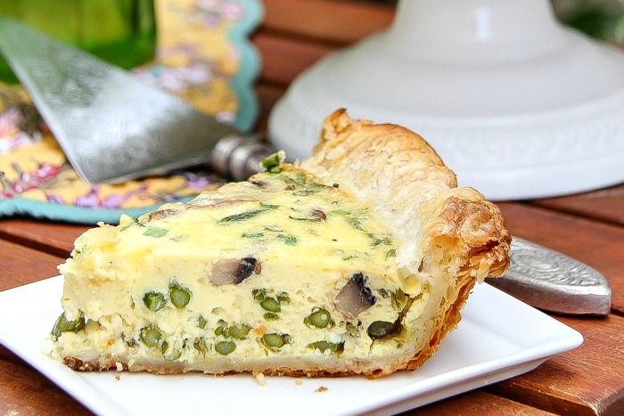 a slice of asparagus and mushroom quiche on a white plate