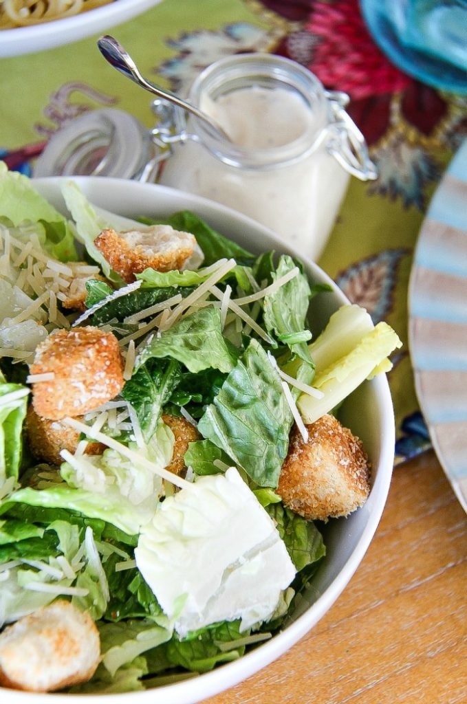 A serving bowl of Caesar salad with a jar of dressing on the side