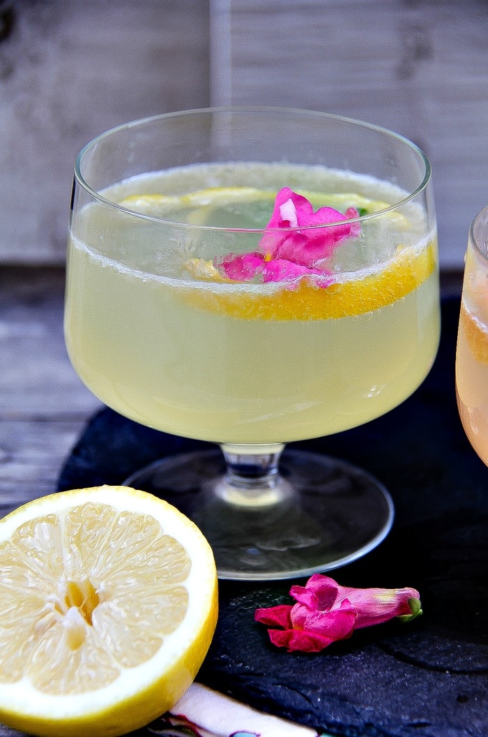 lemon cocktail with gin and prosecco in a cocktail glass garnished with a pink flower and lemon slice