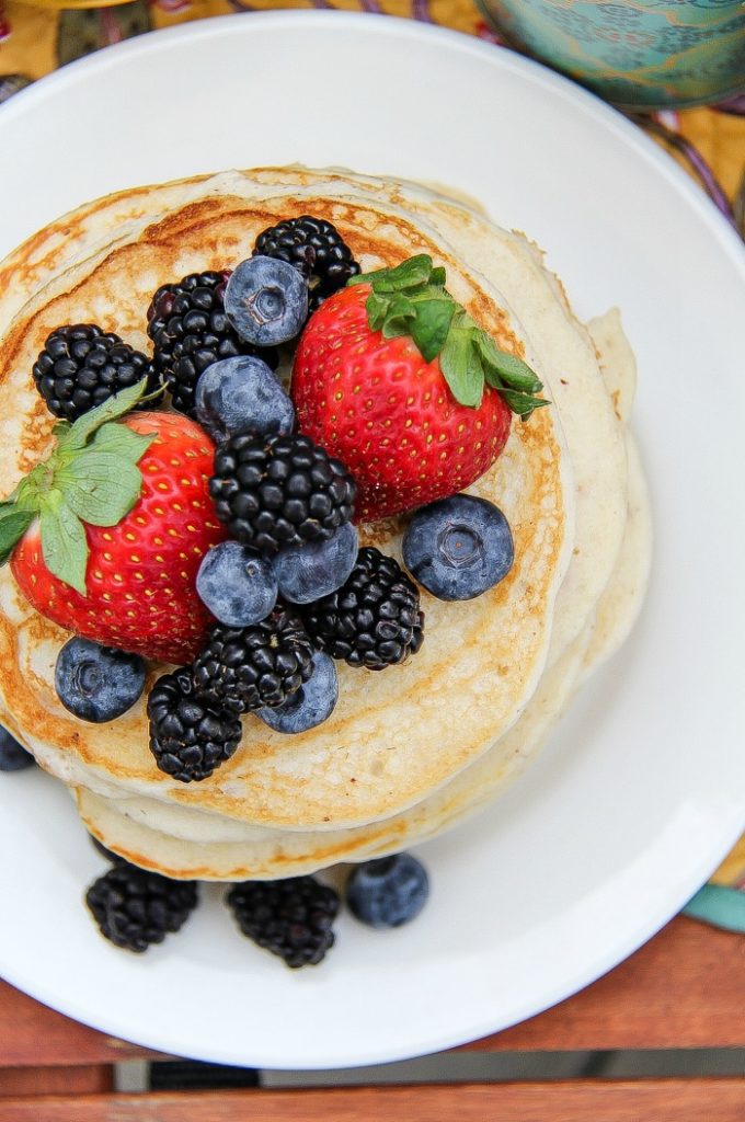 Looking down on a stack of pancakes on a white plate topped with fresh blueberries, blackberries, and strawberries