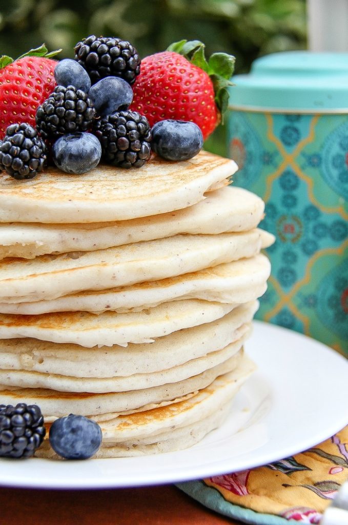 A stack of pancakes on a white plate topped with fresh blueberries, blackberries, and strawberries