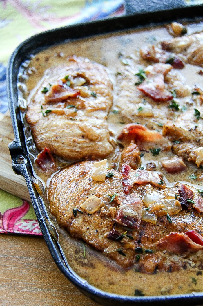 a cast-iron skillet with chicken breasts and bacon in a creamy sauce