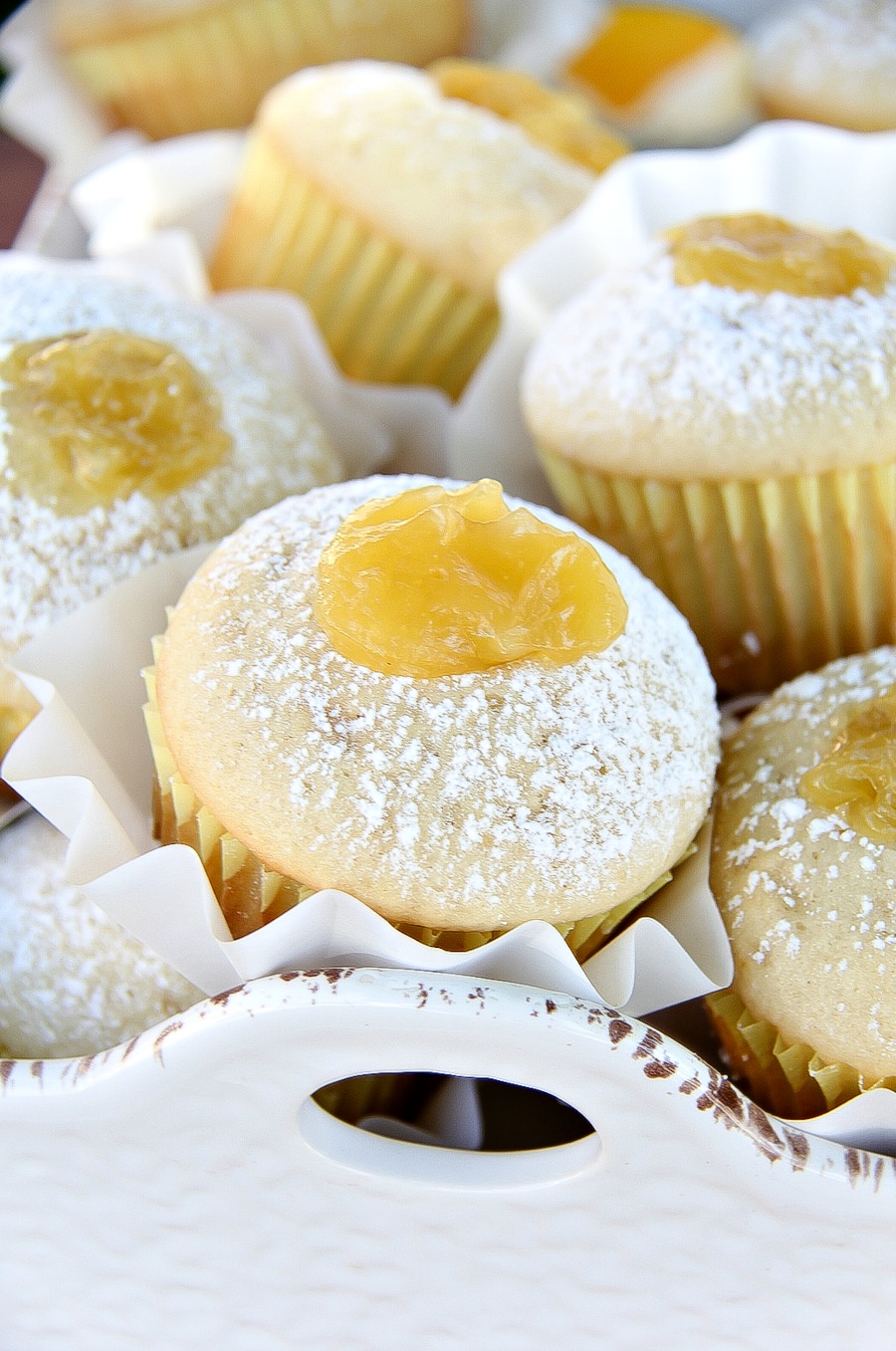 muffins in a white tray with lemon curd on top and confectioners sugar sifted over them