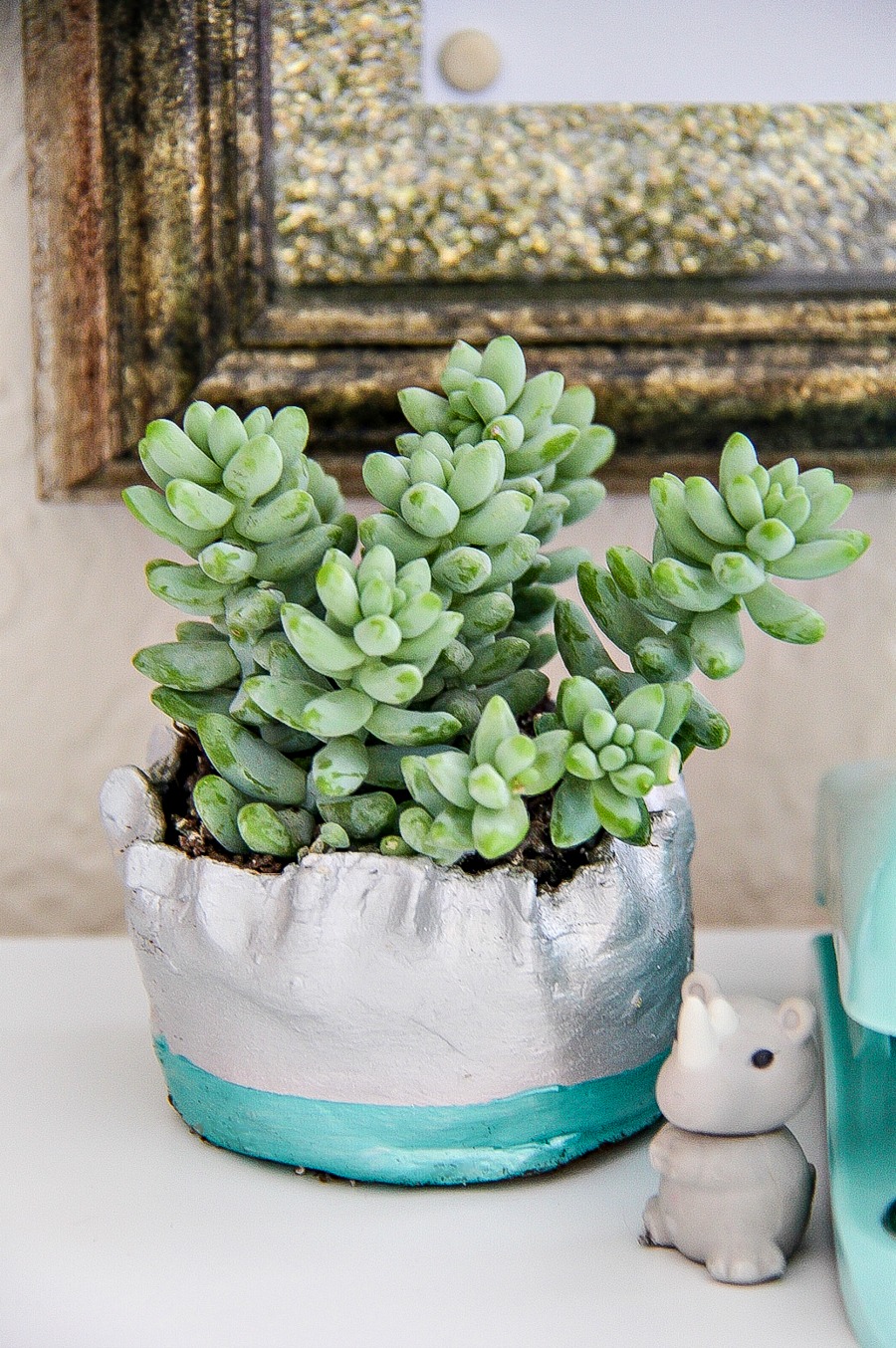 A handmade clay planter painted silver and blue with a succulent planted inside it.