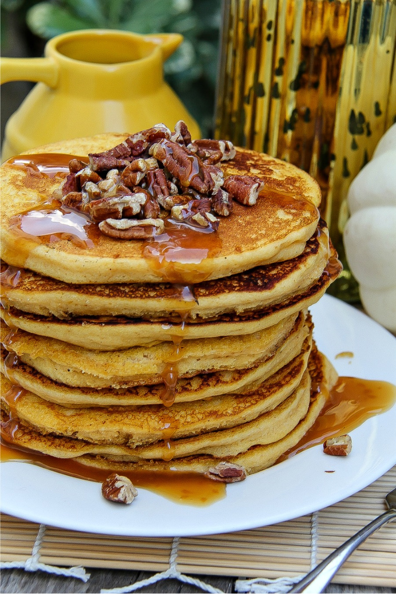 A stack of gluten-free pumpkin pancakes with syrup and chopped pecans.