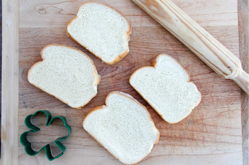 Bread being rolled with a rolling pin and cut with a shamrock cookie cutter.