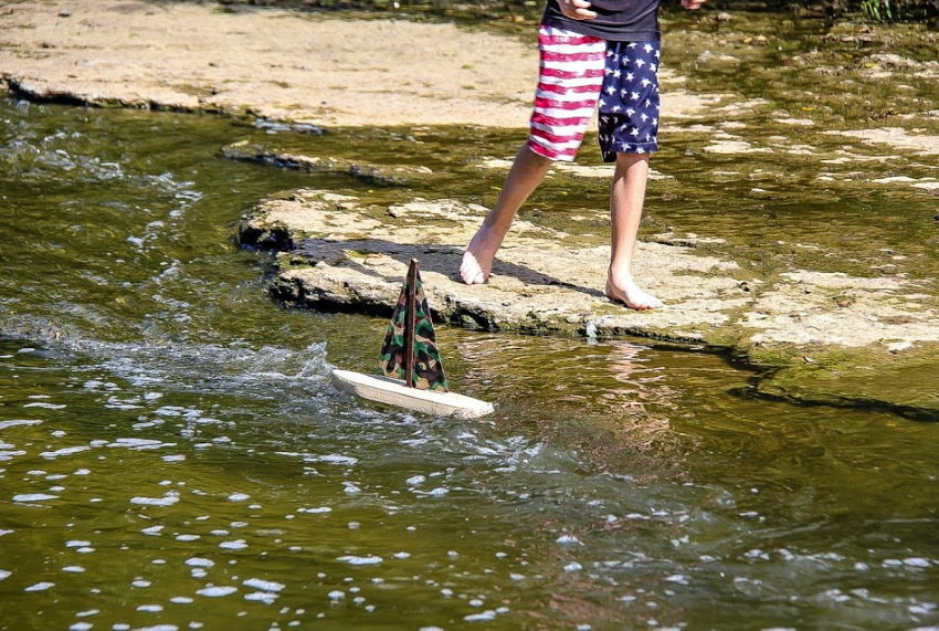 A boy playing with a handmade sailboat on a creek.