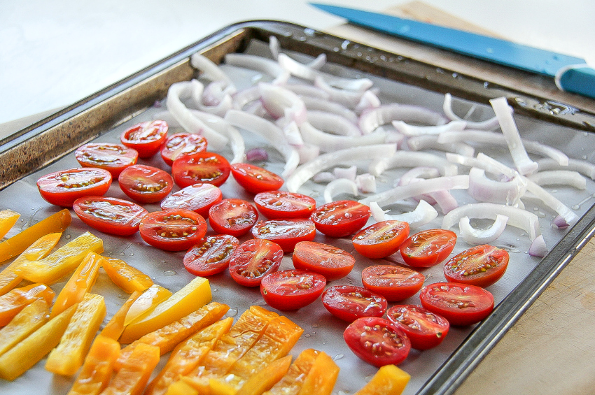 tomatoes, peppers, and red onions on a tray for roasting.