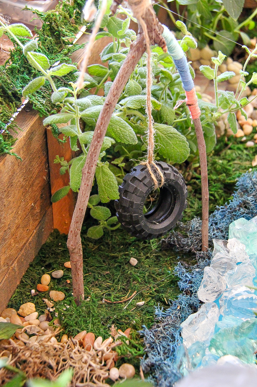 A tire swing for a fairy garden made out of a toy tire from a car and a stick wrapped with string.