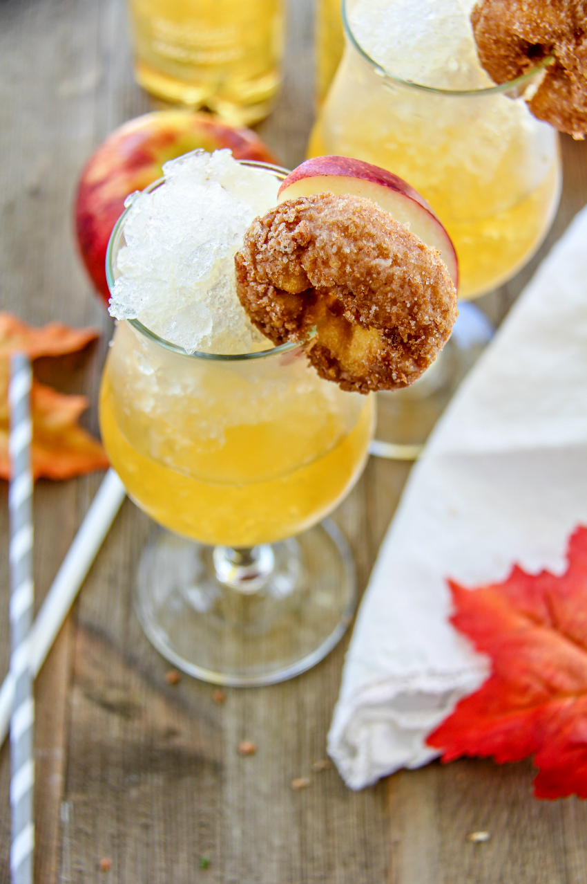 A cinnamon apple slush in a glass and garnished with an apple slice and cinnamon donut.