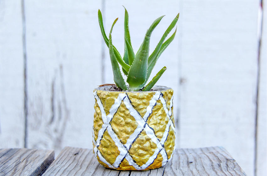 A pot painted like a pineapple with a succulent planted inside. 