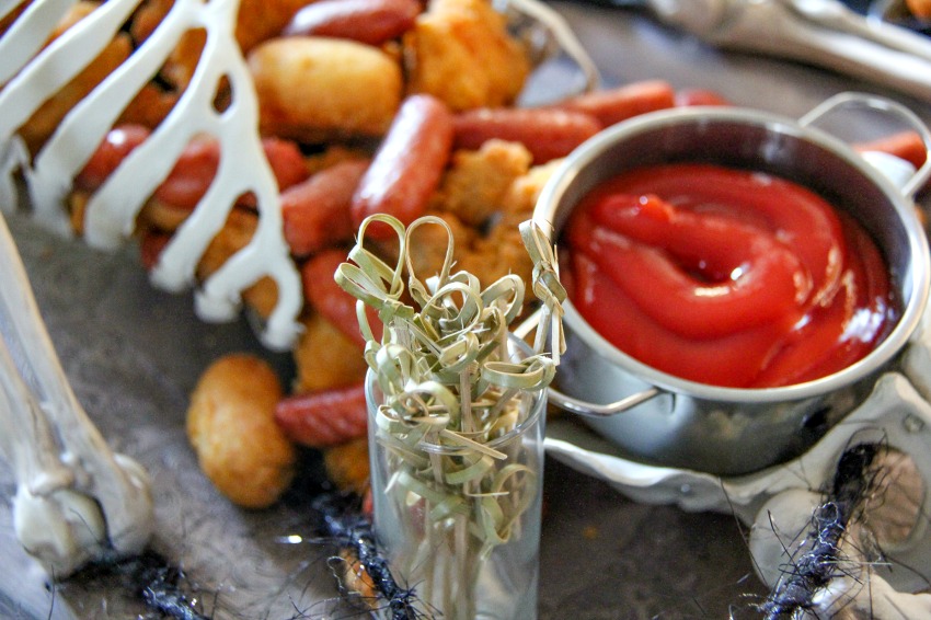 A skeleton party tray with party picks and ketchup 'blood'.
