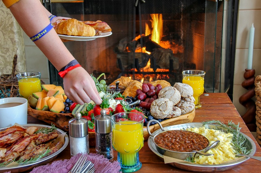 A grazing platter for brunch including fruit, bacon and eggs, biscuits, croissants, and coffee.