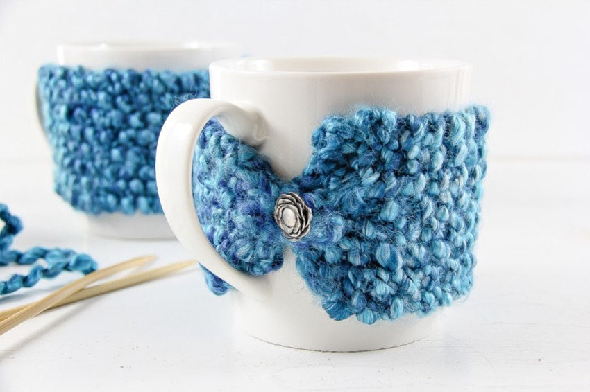 knit coffee mug cozy pattern using blue yarn and a button.
