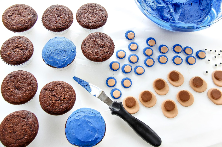 Blue frosting being spread onto chocolate cupcakes.
