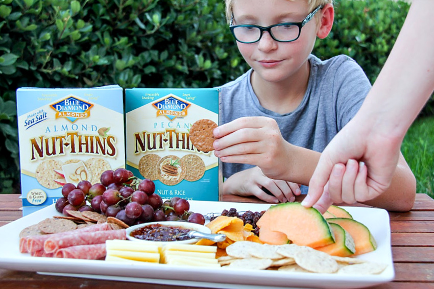 A kid with a gluten-free charcuterie board that has Blue Diamond Nut Thins.