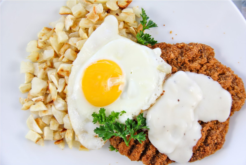 Country fried steak with fried potatoes and an egg.