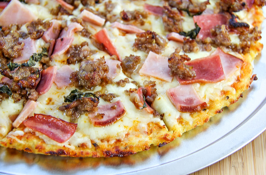 Cauliflower pizza crust topped with ham, bacon, and sausage. 