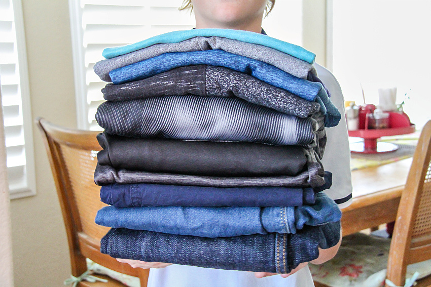 a boy holding a stack of blue and grey clothes