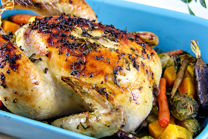 a whole roast chicken with vegetables in a blue baking dish