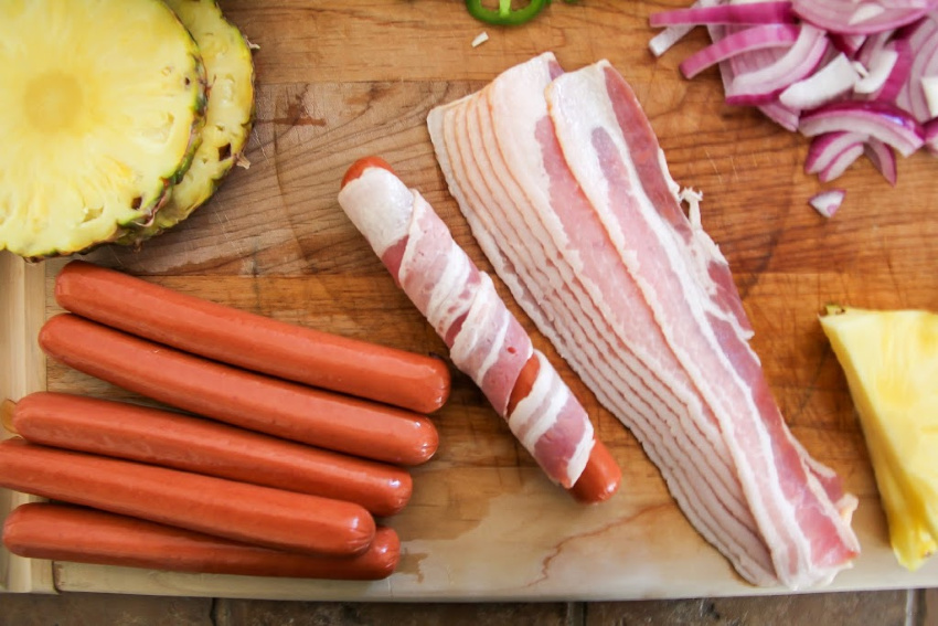 hot dogs on a cutting board being wrapped in bacon