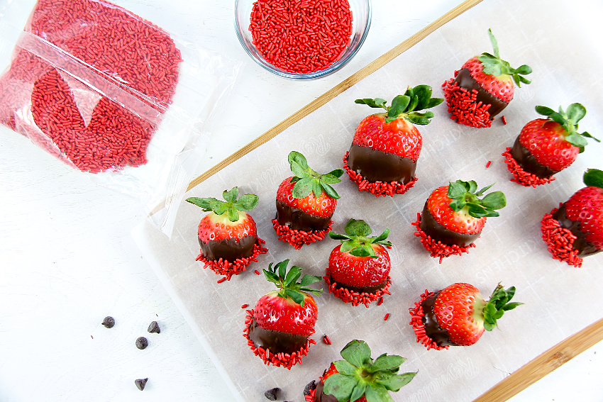 chocolate covered strawberries on parchment paper with red candy sprinkles