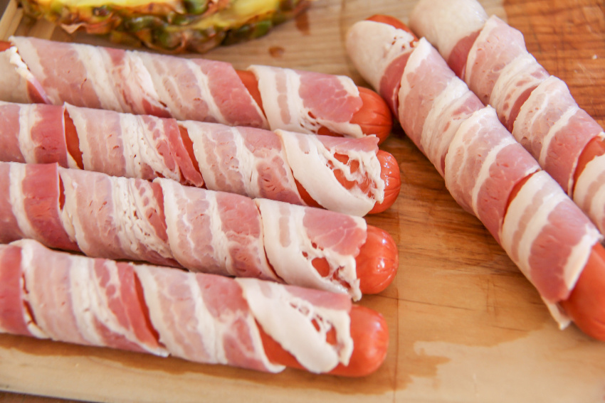 hot dogs being wrapped in bacon to be cooked on the grill