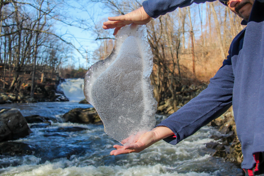 man holding block of ice in front of a waterfall