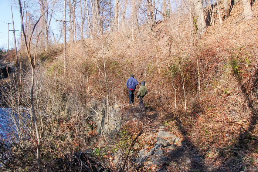 Outdoor winter activities in New Jersey for families. A man and boy walking along cliff edge through brush and barren trees