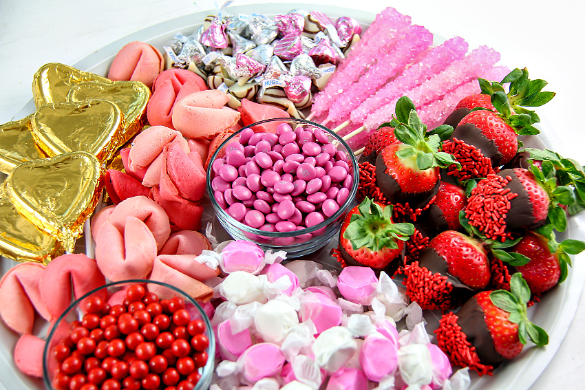 a candy tray for Valentine's Day filled with fortune cookies, chocolate covered strawberries and pink candies.