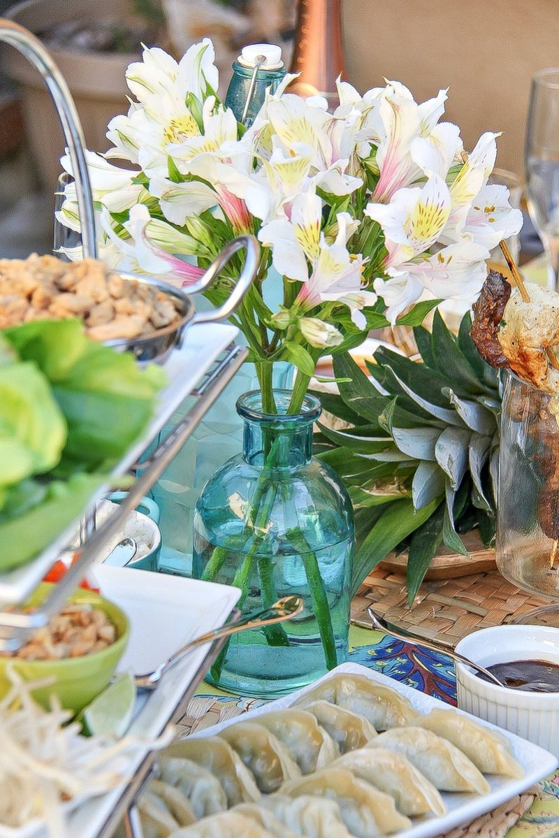 a blue vase with white flowers on an outdoor table surrounded by Asian food