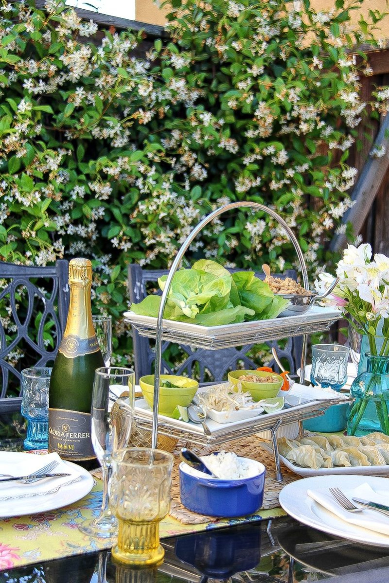 An outdoor dining table with a tiered tray containing ingredients to make lettuce wraps