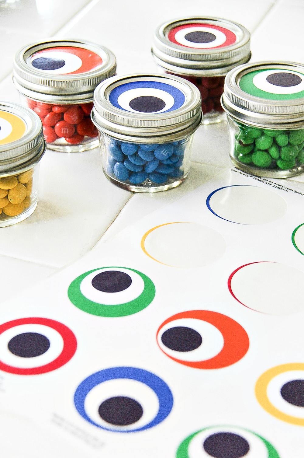 small canning jars filled with colorful candy with monster eye round labels to go on top