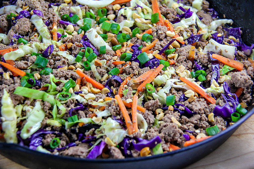 ground turkey, cabbage, and carrots in a cast-iron skillet with green onions and chopped peanuts on top