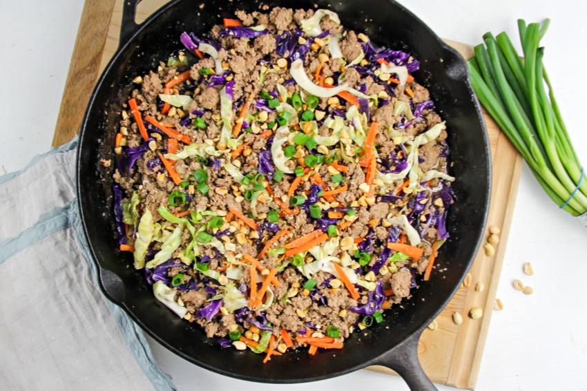 a cast iron skillet on a cutting board with a ground turkey stir fry with cabbage 