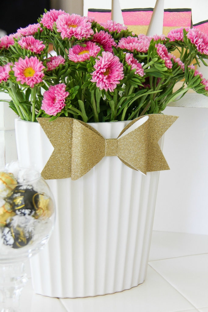 a gold glitter bow on a white vase filled with pink flowers