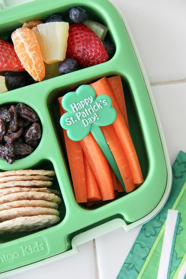 a rainbow of fruit with carrot sticks and a st patricks day pick in a lunch box