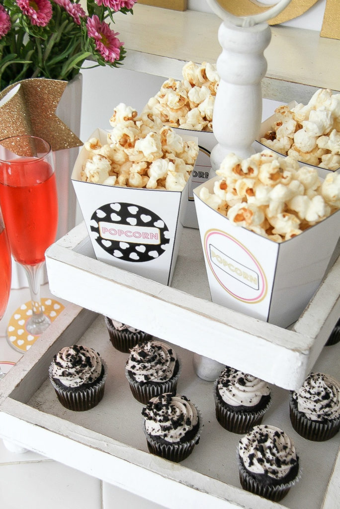 a white tiered wood food stand containing popcorn and cupcakes