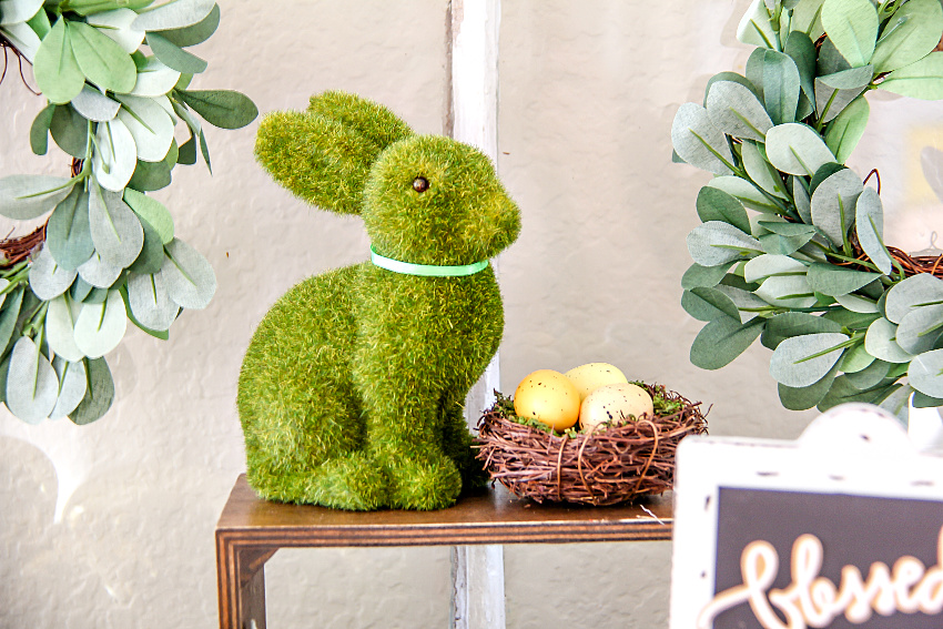 moss green bunny on a wood stand with a nest of eggs