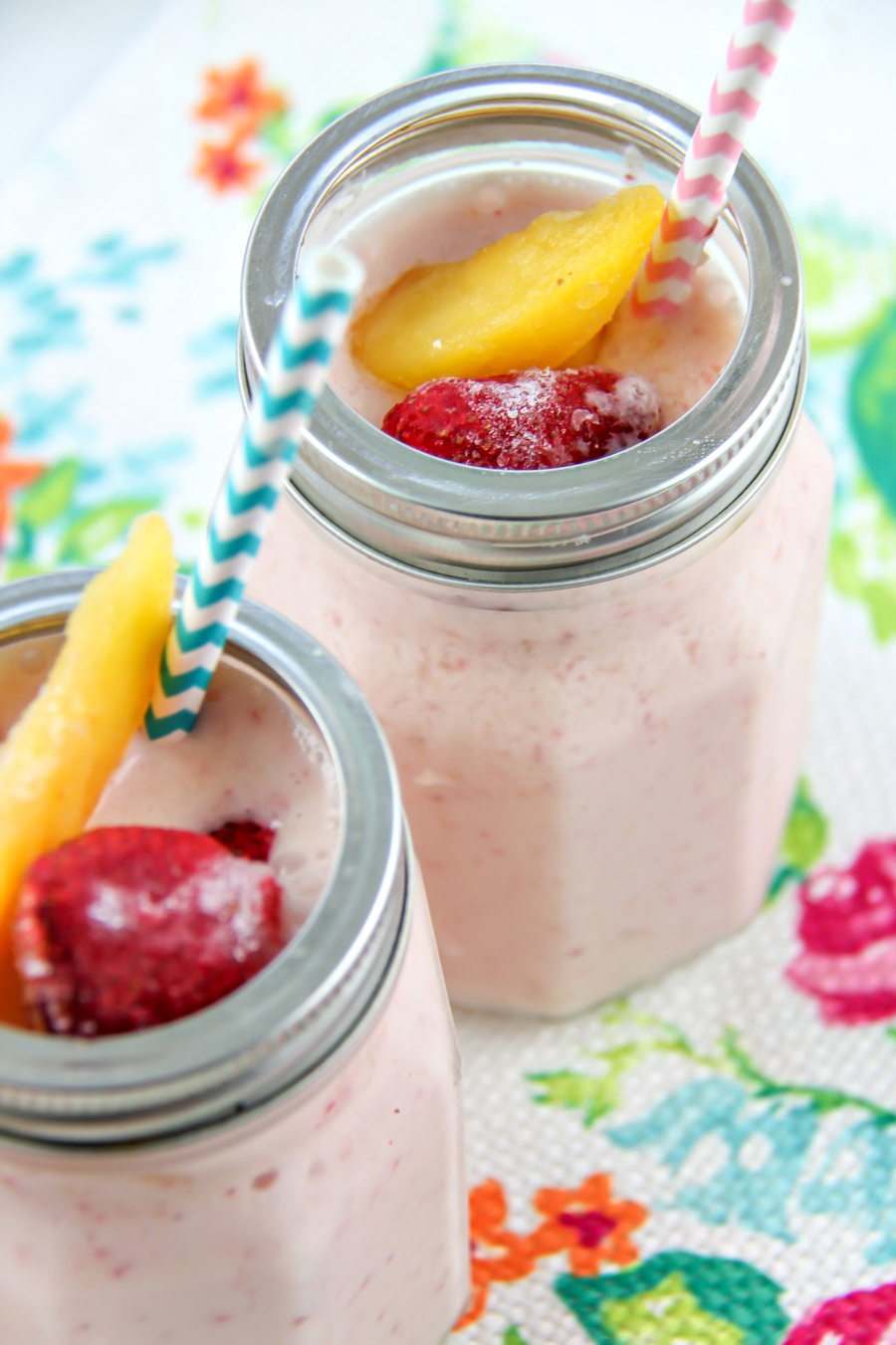 a pink smoothie in a glass jar with frozen strawberry and mango on top