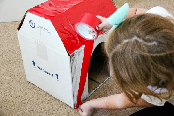 a girl covering a cardboard box in red duck tape