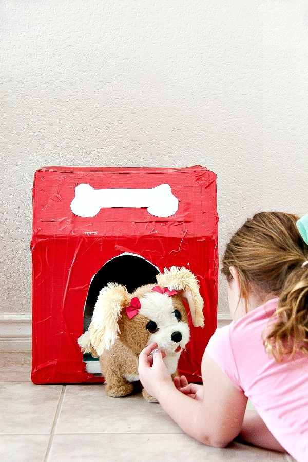 a girl playing with a toy dog in front of a cardboard and duck tape kennel she made