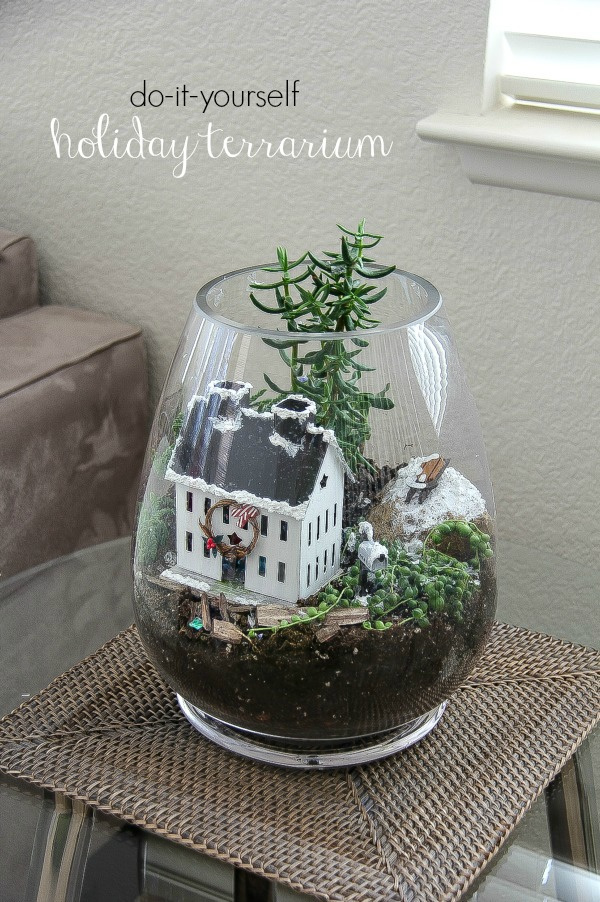 a christmas terrarium with plants, snow, and a house inside