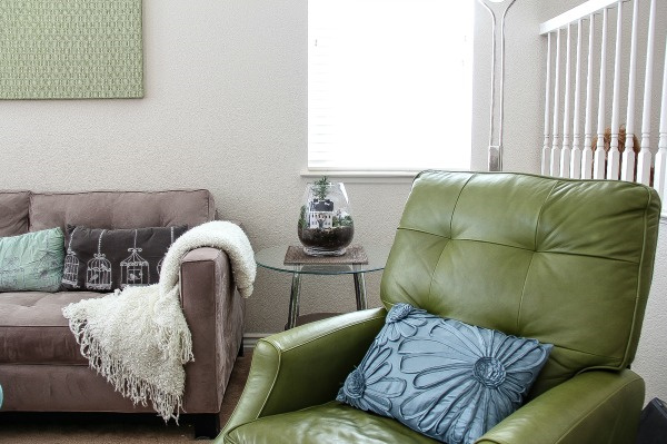 a green chair, sofa, cushions, and a christmas terrarium on a side table