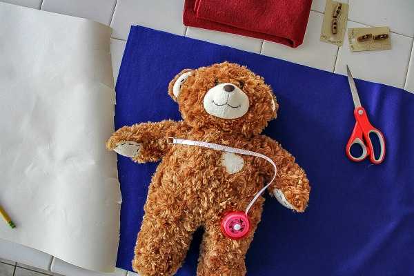 a teddy bear lying on blue felt to take measurements for making a coat