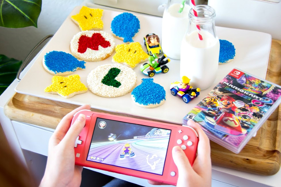 girls hands holding a coral nintendo switch lite with mario kart party treats on a white tray